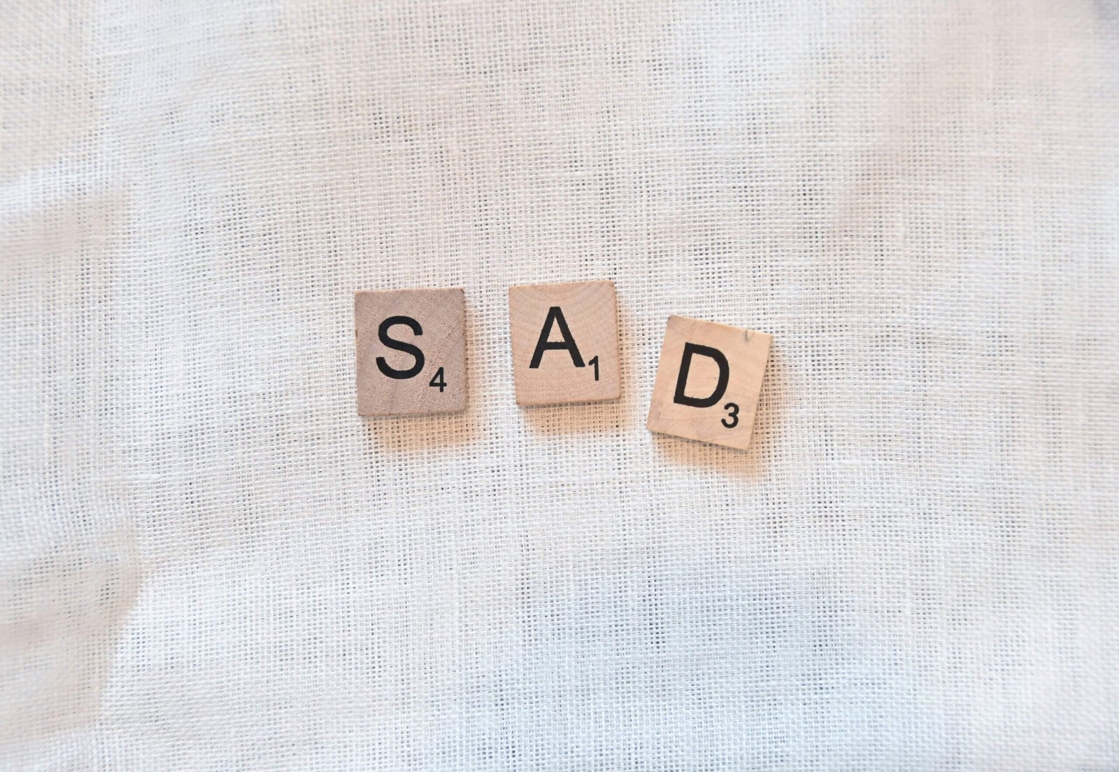 Mot SAD épelé avec des lettres de scrabble sur un tissu blanc – symbole de tristesse douce et introspective
